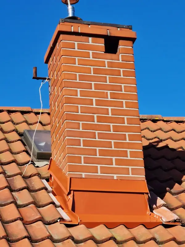 Obróbka blacharska komina klinkierowego wykonana z blachy powlekanej w kolorze ceglastym. Tradycyjna metoda rzemieślnicza zamiast taśm kominowych gwarantuje spokój na lata.