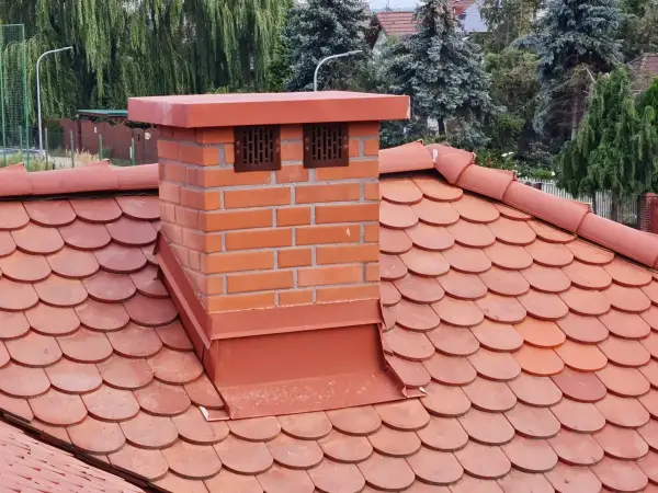 Obróbki blacharskie i czapa komina z blachy powlekanej w kolorze ceglastym,  idealnie pasują do komina murowanego z klinkieru.